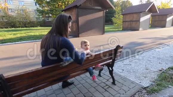 小女孩在公园里吃饭妈妈给婴儿水果妈妈和女儿坐在长凳上视频的预览图