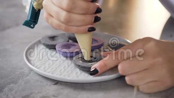近距离拍摄女人的手使用糕点袋在一半的马卡龙上涂上奶油视频的预览图