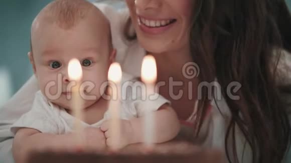 妈妈带着婴儿吹生日蜡烛带着孩子在蛋糕上吹蜡烛的女人视频的预览图