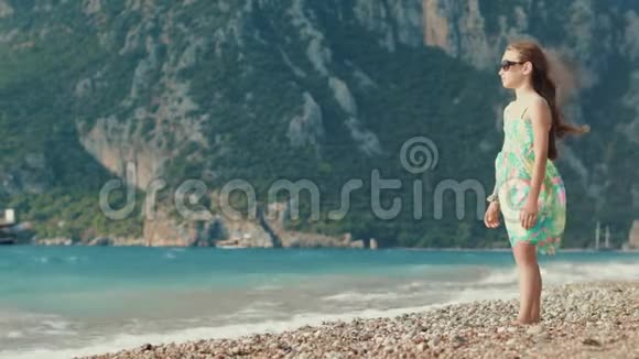 年轻的女孩在海边和山对着思考儿童在海滩上放松视频的预览图