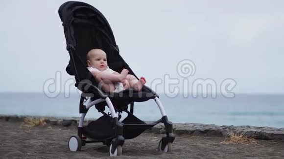 在沙滩上的婴儿车里怀着极大的兴趣安详地凝视着无限和海浪享受着迟来的时光视频的预览图