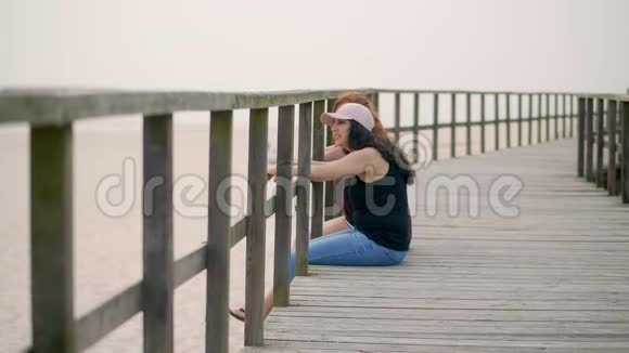 年轻女子坐在沙滩上的木墩上视频的预览图