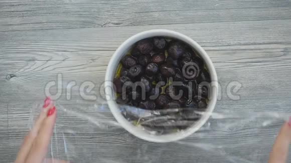 将黑色橄榄包装在木桌上的食品薄膜中视频的预览图