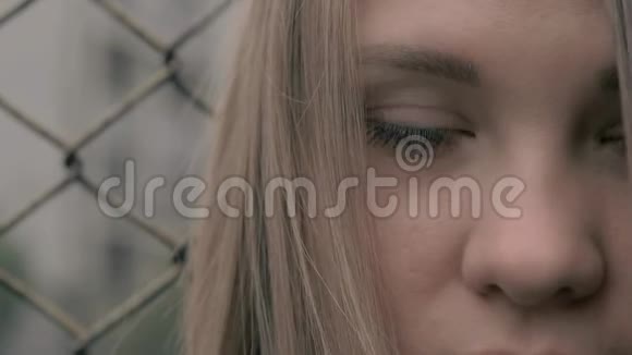 忧郁和悲伤的金发欧洲女孩的肖像背景是铁栅栏在金属面前的年轻女子视频的预览图