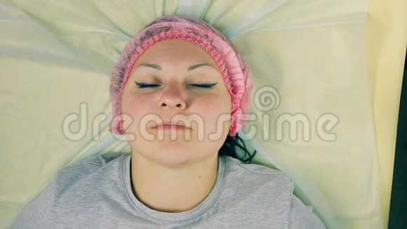 化妆师的男人的手从躺在沙发上的女人的头上取下化妆帽视频的预览图