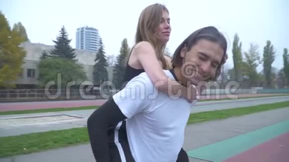 穿运动服的帅哥背着一个女孩漂亮的年轻夫妇在户外运动服装视频的预览图