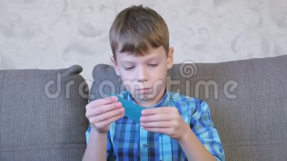 快乐的男孩正在伸展一个蓝色的黏液坐在教练上玩视频的预览图