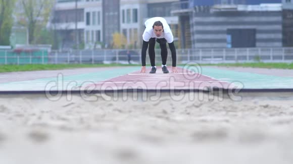 穿着运动服的年轻人在镜头前的沙子里加速跳跃沙子从一个人脚下散落下来视频的预览图