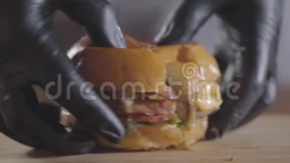 厨师的双手戴着黑色橡胶手套压着一半的汉堡和酱汁流出特写美味的食物视频的预览图