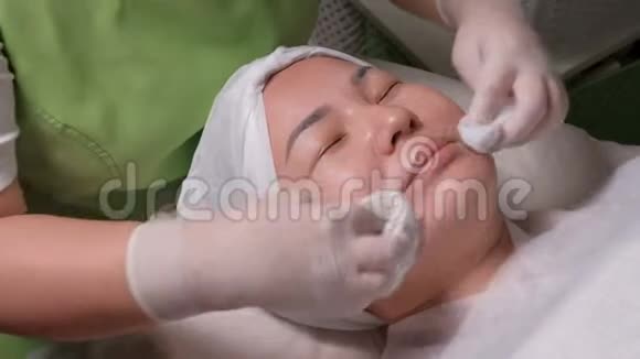 职业美容师戴着白手套的双手用化妆巾擦拭一个放松的穆斯林女人的脸特写镜头东视频的预览图