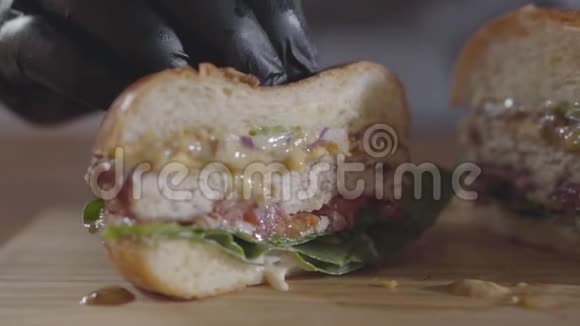 厨师的特写双手戴着黑色橡胶手套压着一半的汉堡和酱汁流出美味的食物视频的预览图