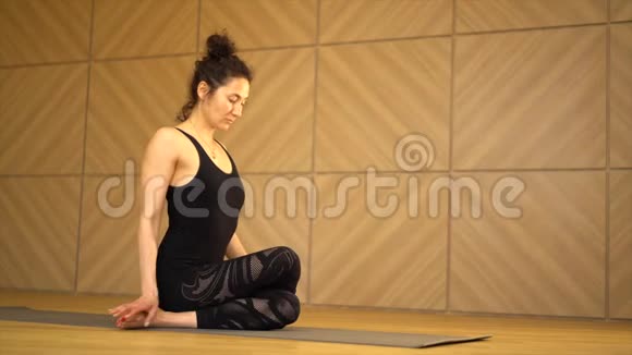 年轻漂亮的女人在灯光极简主义工作室教室练习瑜伽坐着做伸展运动的女孩视频的预览图
