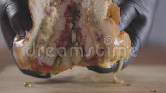 厨师的特写双手戴着黑色橡胶手套压着一半的汉堡和酱汁流出美味的食物视频的预览图