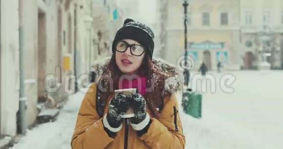 手里拿着咖啡的女孩走过一个下雪城市的街道视频的预览图