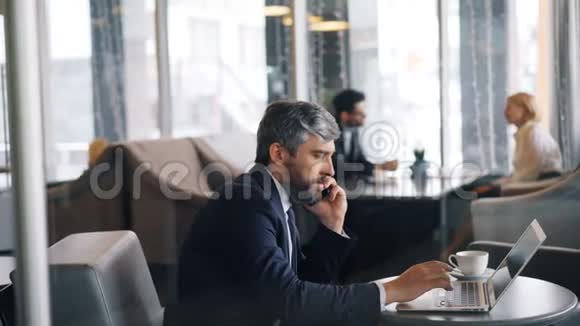 企业家用手机和笔记本电脑在咖啡馆工作视频的预览图
