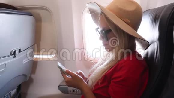 日落时分戴着帽子的游客坐在飞机窗户附近飞行时使用手机视频的预览图