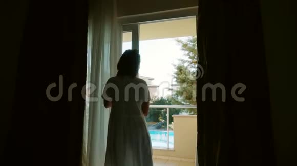 一个穿着白色连衣裙的女人打开门走向阳台视频的预览图