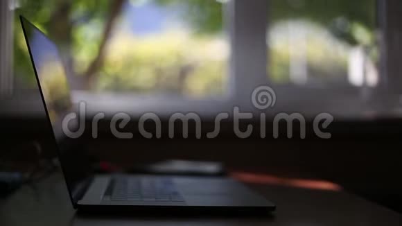 家用木制桌子上的现代笔记本电脑带有bokeh的窗口背景视频的预览图
