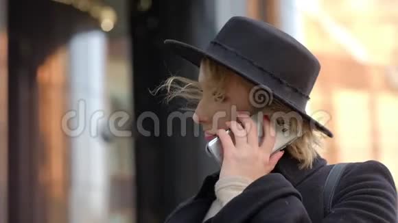 戴着黑帽子的漂亮女孩微笑着在智能手机特写上交谈视频的预览图