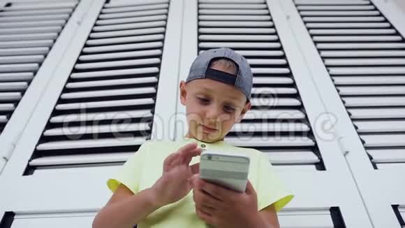 小男孩玩游戏时使用手机的特写穿T恤的可爱男孩打字留言的肖像视频的预览图