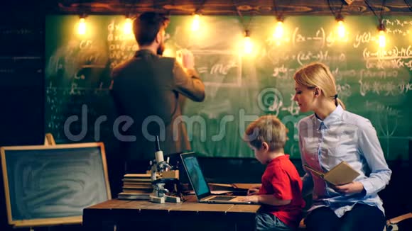 小男孩在笔记本电脑上看动画片妈妈坐在学校教室里黑板上写着视频的预览图