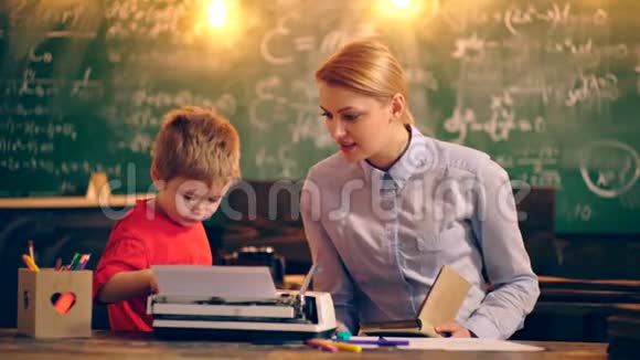一个男孩带着老师在学校教室里的一台打字机上打字背景是一块绿色的木板学习概念视频的预览图