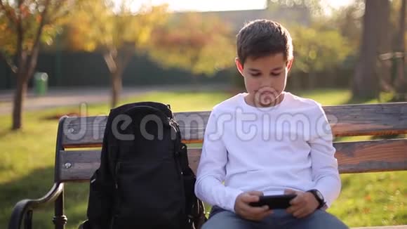 放学后十几岁的男孩在公园的智能手机上玩网络游戏视频的预览图