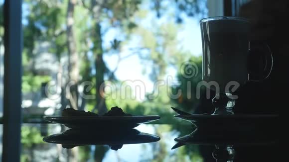 未被识别的女人剪影喝着咖啡和蛋糕背景的漂亮窗口视图视频的预览图