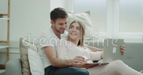 很有魅力的一对夫妇微笑着早上在沙发上两人都穿着睡衣从笔记本上订了一份视频的预览图