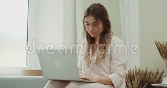早上一位穿着粉红色睡衣的女士在客厅的笔记本上工作现代设计视频的预览图