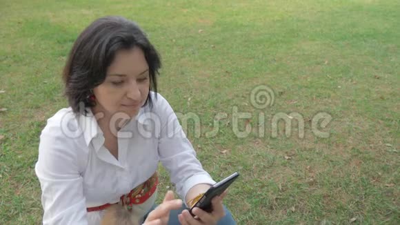 一个中年妇女在空地上休息的肖像并在她的手机上读取信息视频的预览图