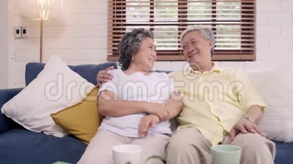 在家里客厅的沙发上放松时亚洲老年夫妇感到快乐的微笑和看着相机视频的预览图