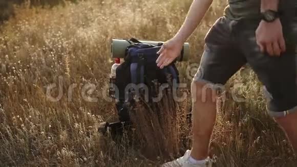 年轻人徒步旅行从地上捡起他的背包山上干草穿着牛仔衬衫和T恤视频的预览图