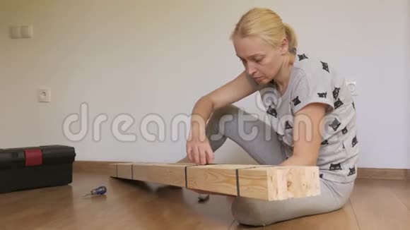 一个女人坐在地板上的房间里打开商店里买的木架家具组装视频的预览图