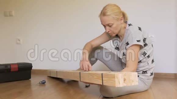 一个女人坐在地板上的房间里打开商店里买的木架家具组装视频的预览图