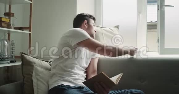 适合一个年轻人在沙发上看书喝咖啡的完美早晨视频的预览图