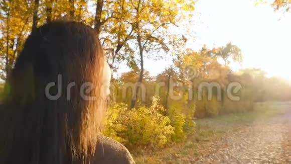 美丽的黑发沿着秋天公园散步环顾四周明亮的阳光特写视频的预览图