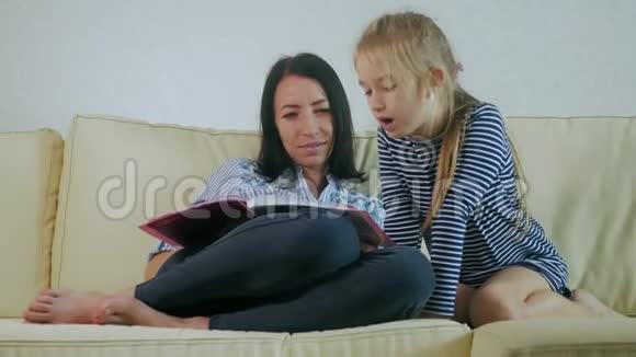 母亲和小女儿在家里的沙发上看书只有母亲和她的小女儿的时间视频的预览图