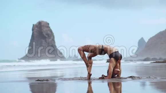 一位身穿泳装的美女在海滩上表演一座运动桥桥上环绕着黑色的火山沙视频的预览图