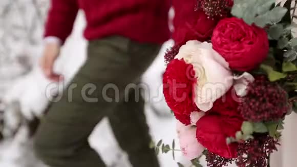 新娘携带一束由白色和红色玫瑰制成的花年轻的新婚夫妇在雪地森林里散步视频的预览图