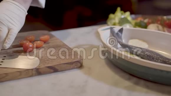 厨师手戴白色橡胶手套用大刀切切樱桃西红柿用鱼和西葫芦紧紧地放进碗里视频的预览图