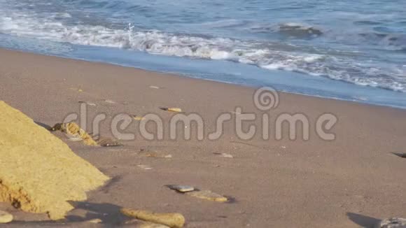 穿着一条蓝色牛仔裤和棕色靴子的年轻人走在美丽海滩的沙滩上视频的预览图