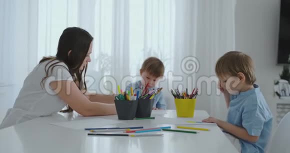 妈妈帮助两个儿子做学前作业在家里的桌子旁画一幅铅笔画视频的预览图