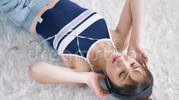 高角度的年轻女子十几岁的少女戴着耳机欣赏最喜欢的音乐躺在白色蓬松的地毯上视频的预览图