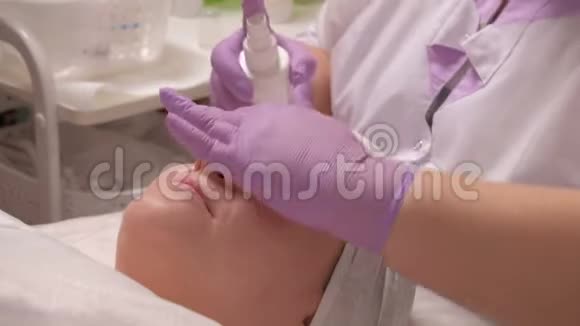 一位戴着紫丁香手套的专业美容师在一位欧洲中年妇女脸上喷洒了一种保湿补品视频的预览图
