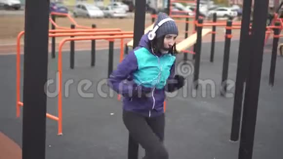 戴着耳机在街头操场上锻炼的女运动员视频的预览图