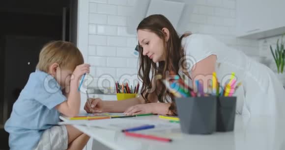 妈妈帮助儿子做学前作业在家里的桌子旁画一幅铅笔画视频的预览图