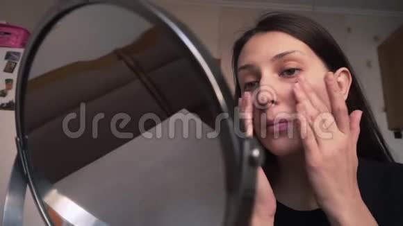 美丽的女孩照镜子在皮肤上涂上遮瑕膏化妆视频的预览图