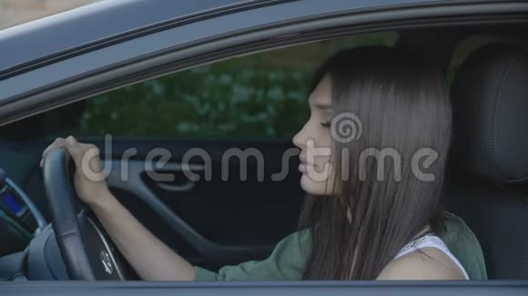 一幅可爱的年轻女子坐在驾驶座的车轮后面的汽车肖像视频的预览图