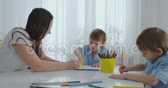 两个男孩的孩子和他的母亲坐在厨房里画画家庭幸福兄弟们在桌子旁画画实际视频的预览图